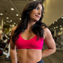 Load image into Gallery viewer, Woman in a pink sports bra and black leggings standing in a gym.
