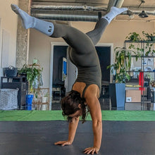Load image into Gallery viewer, Person performing a handstand in a room with plants and furniture.
